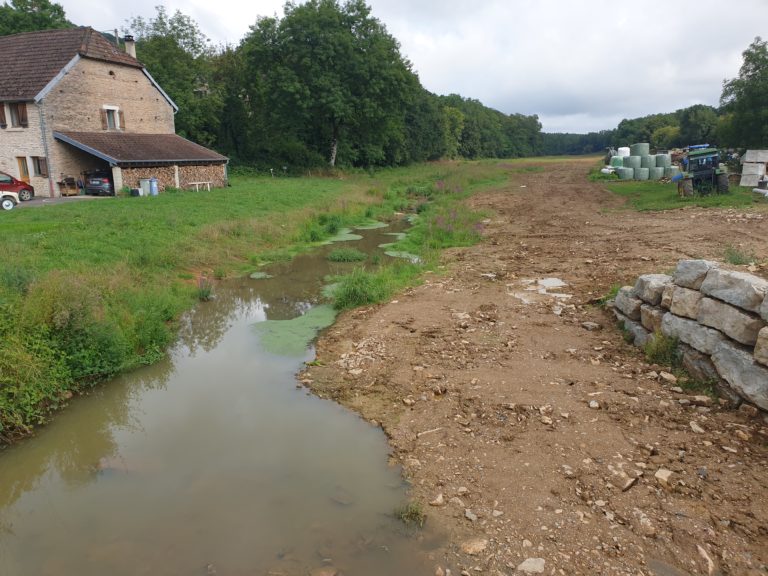 Vue sur l'aval du pont immédiatement après les travaux. on reconnait une rivière connective, méandriforme dès l'aval des habitations, avec un gabarit adapté à l'étiage.